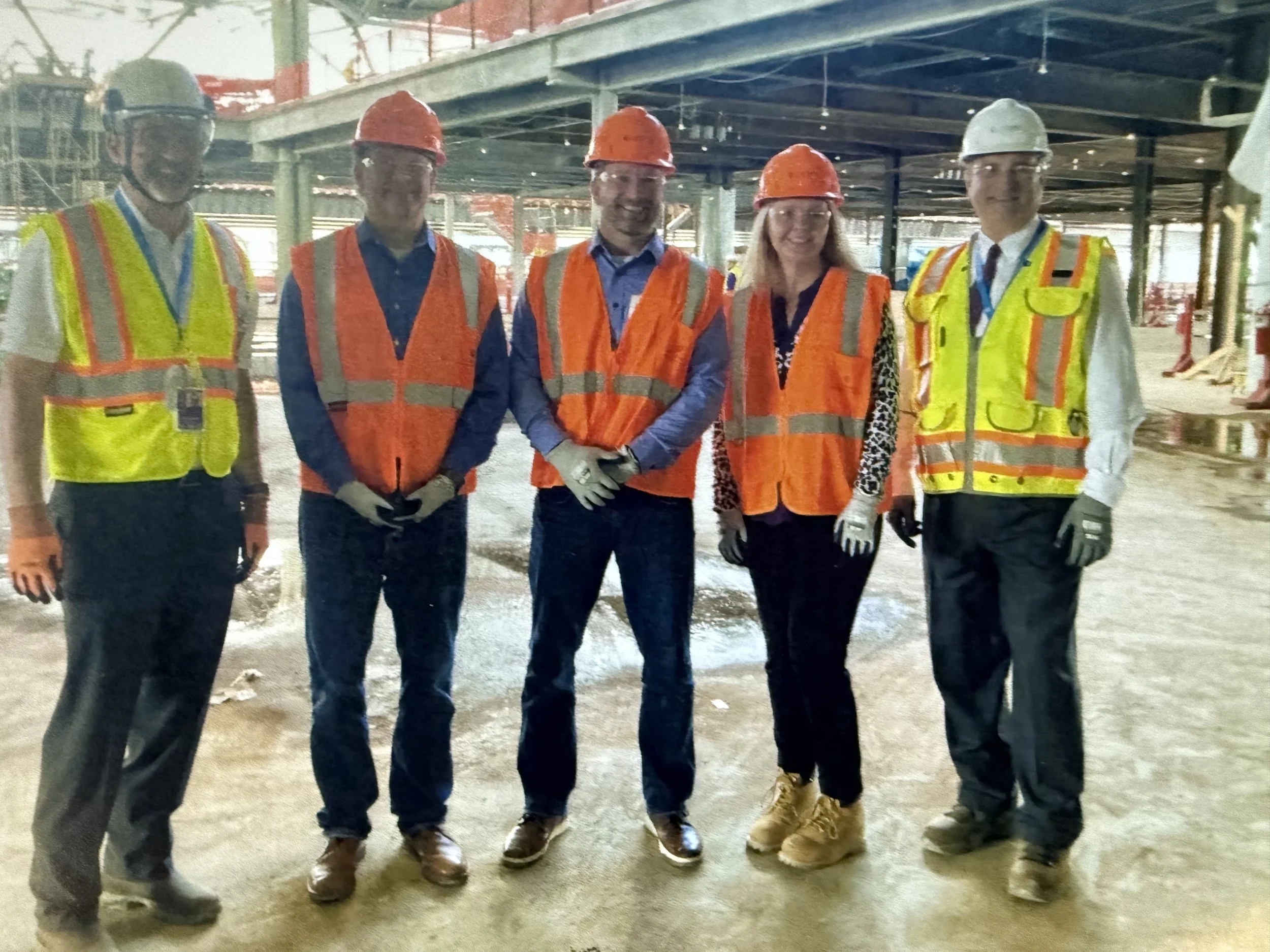 Group of five construction professionals wearing safety vests and helmets at a construction site.