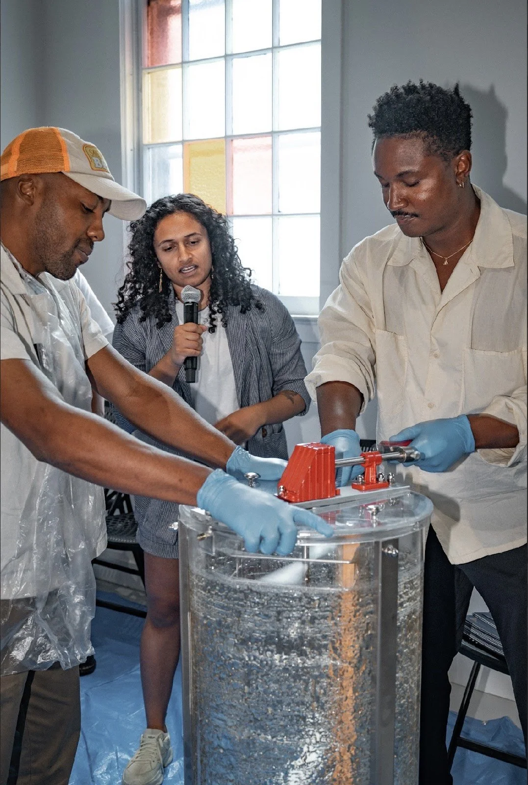 Three people working on a scientific experiment with a large transparent honey extractor at the BEE U graduation