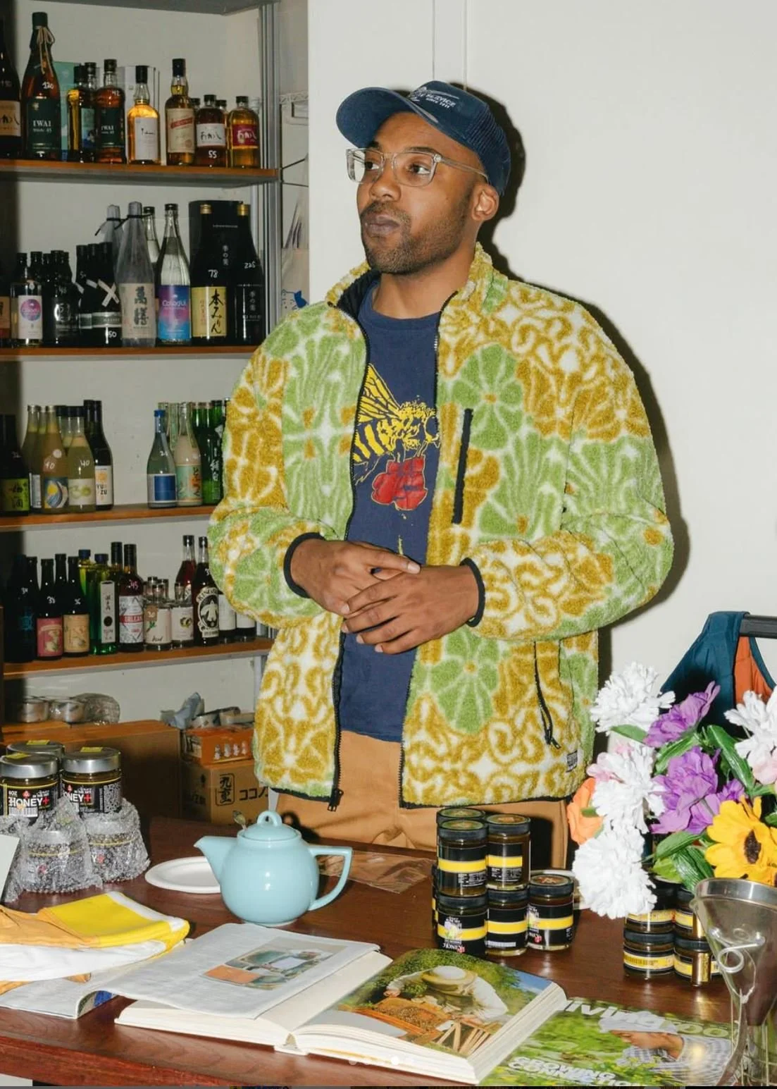 Founder Marcellis Counts  standing behind a table with various jars, a teapot, magazines, and a bouquet of flowers vending at a food and networking event!