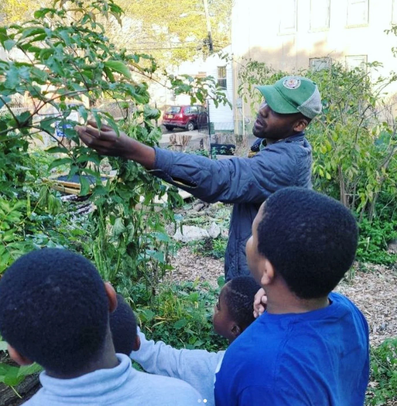 Founder, Marcellis Counts  demonstrating planting or pruning a shrub to a group of children in a garden.
