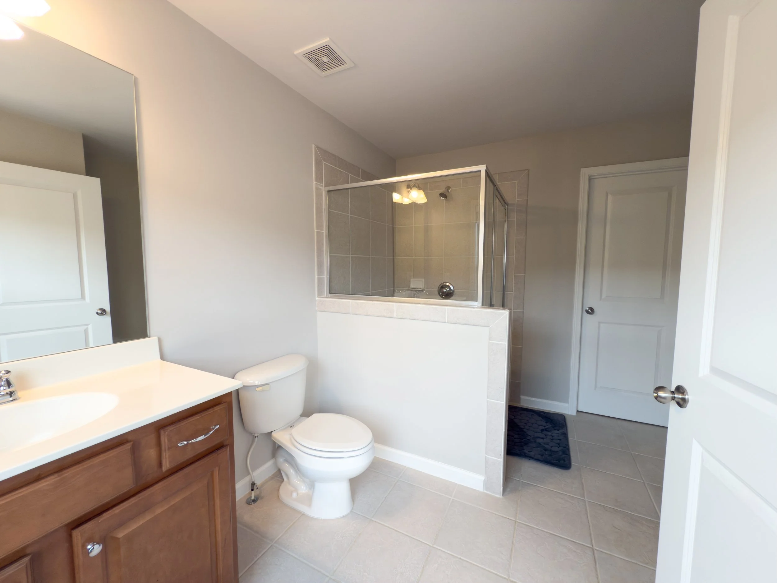 Large ensuite bath for second bedroom with walk-in shower, single vanity, tile flooring, bright front-facing window, and connected walk-in closet.
