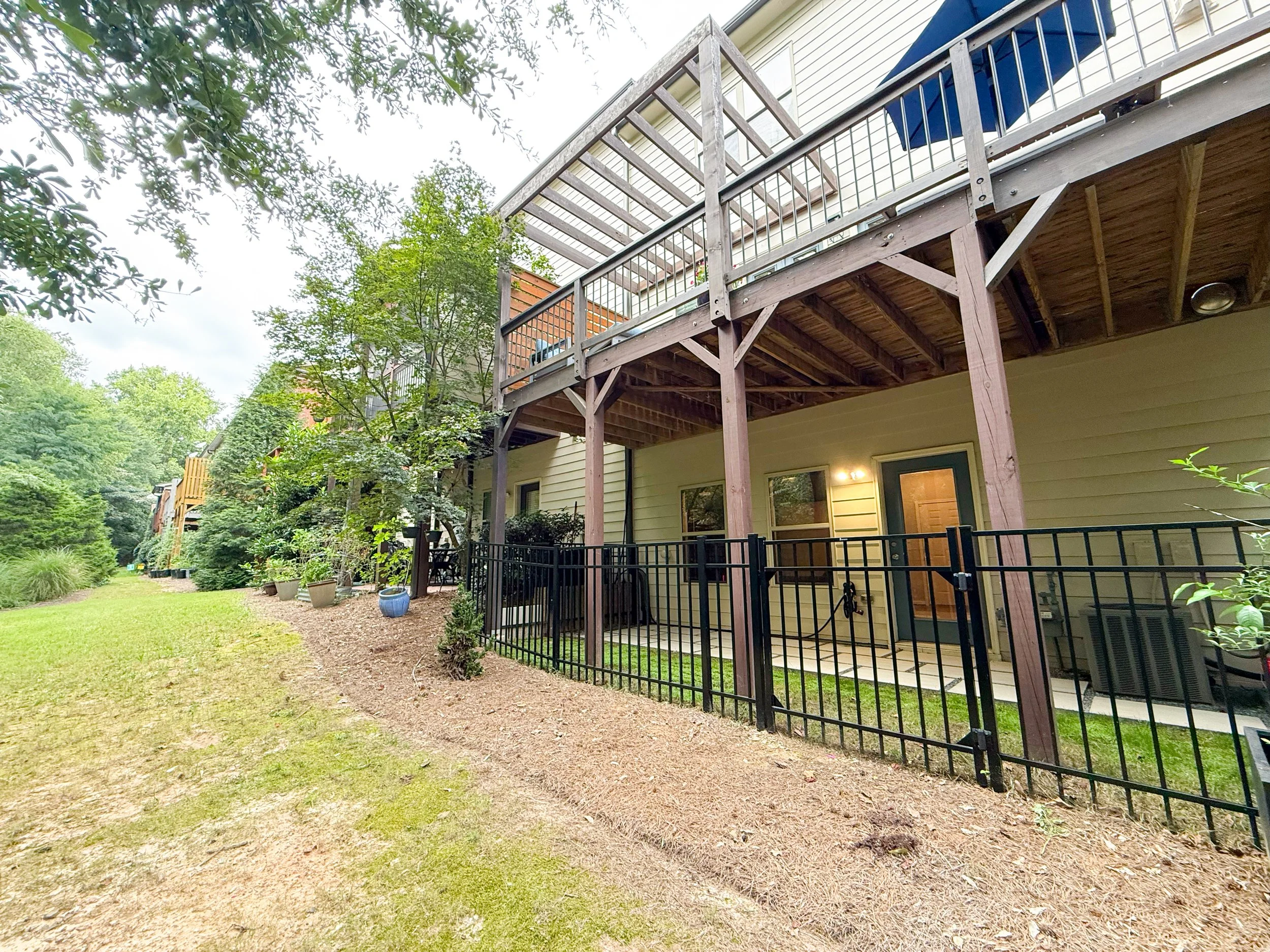 Patio with modern pavers and grass, fully fenced for pets, overlooking peaceful woods and shared green space.