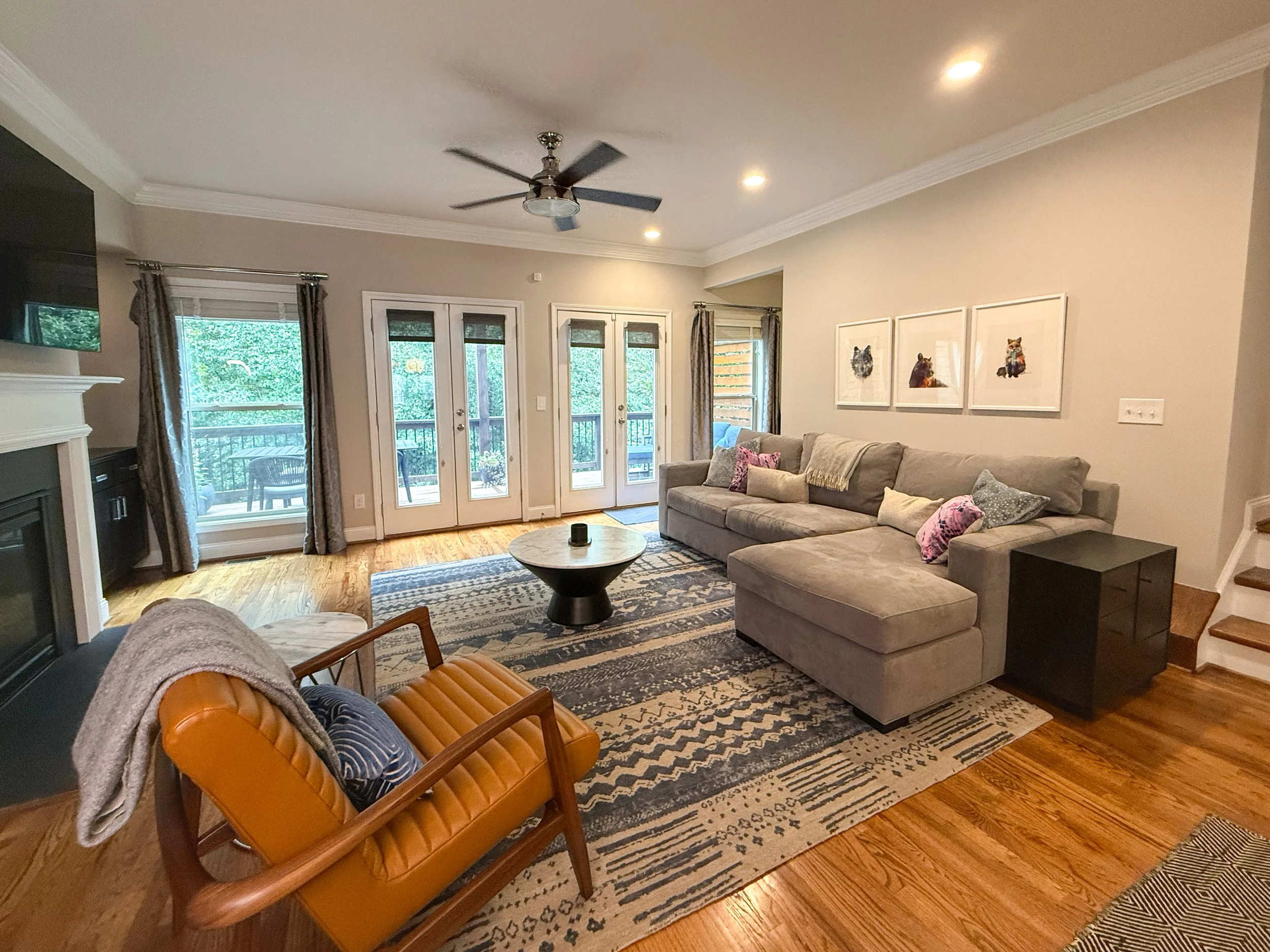 Spacious living room with two sets of French doors to the deck, gas fireplace with TV above, and custom built-ins with floating shelves