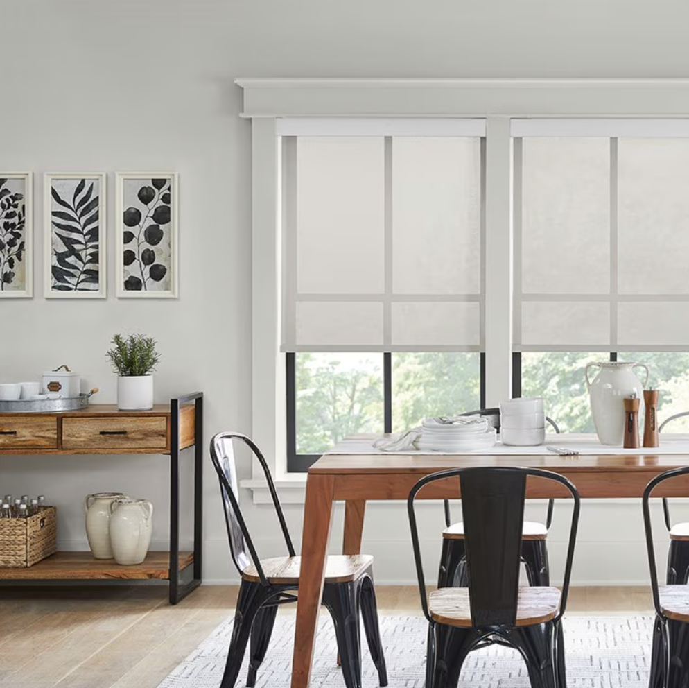 A dining room with a wooden table, black chairs, and a side shelving unit, featuring window blinds and decor.