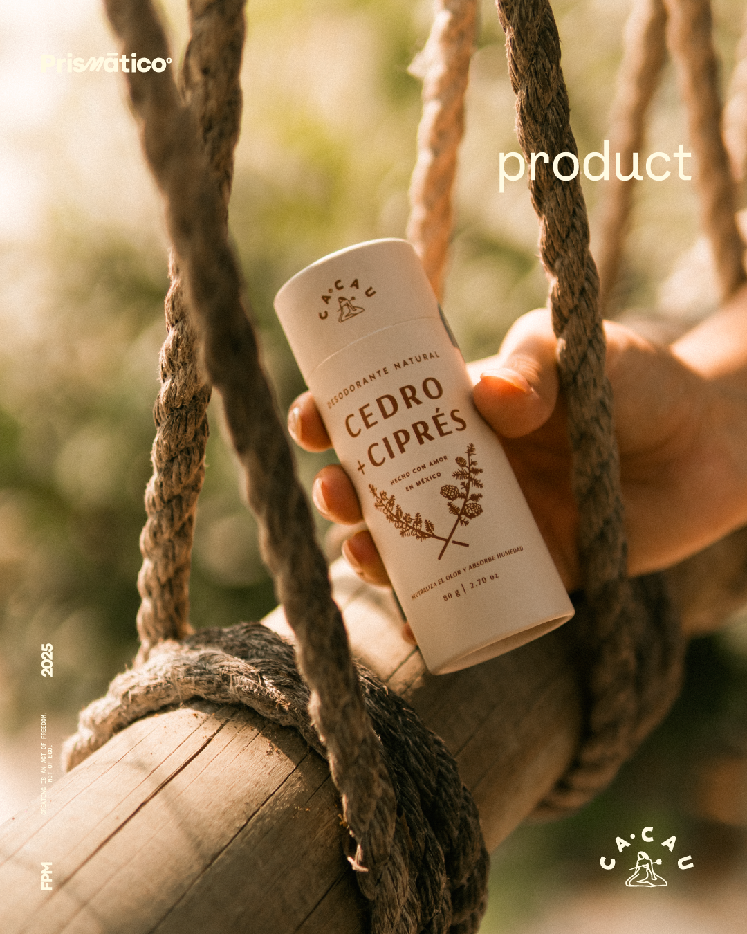 Hand holding a white cylindrical container of Cedro Ciprés natural deodorant against a blurred natural background, with thick ropes and a wooden beam nearby.