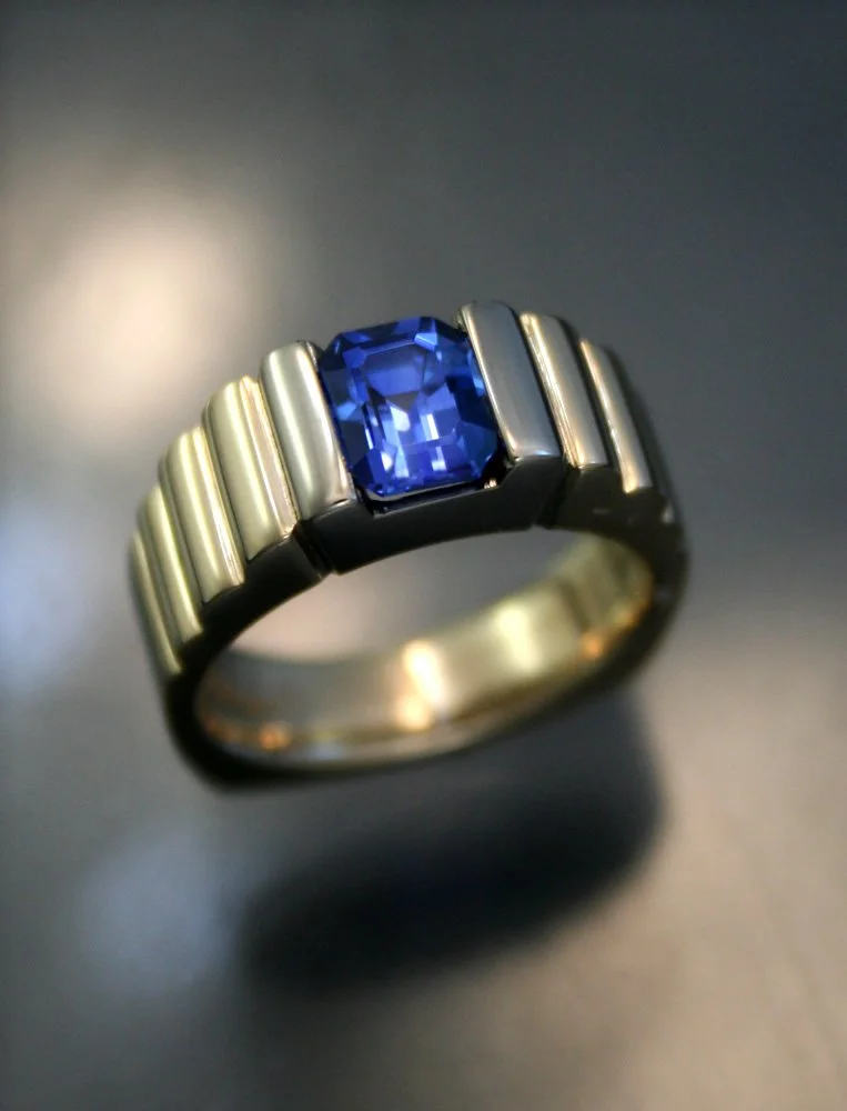 A ring with a rectangular blue gemstone set in a gold band with silver accents.