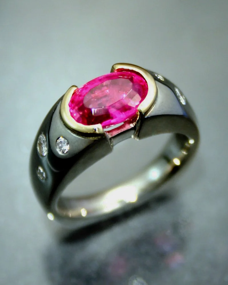 A silver ring with a large pink oval gemstone in the center and small clear stones on the band.