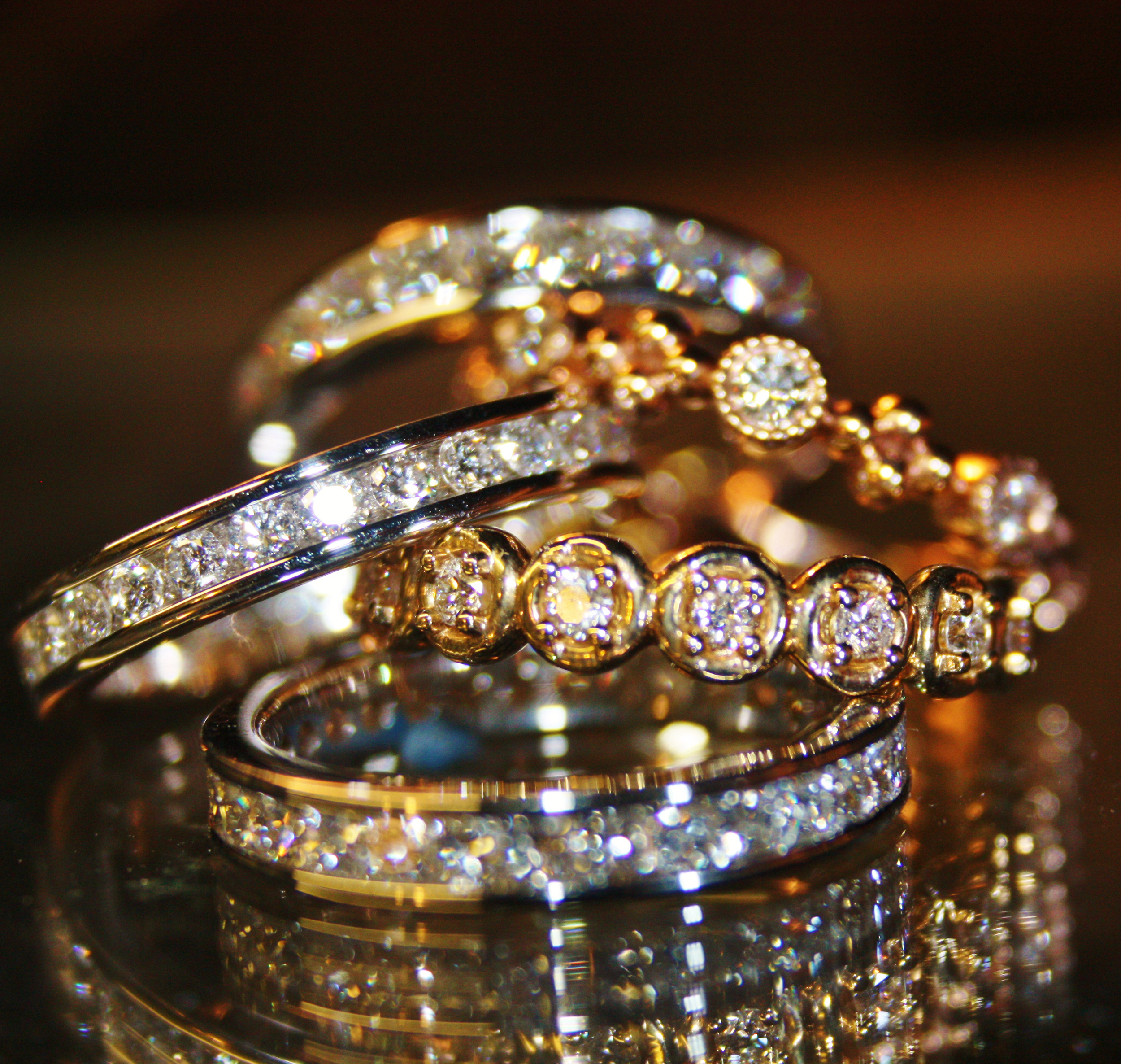Close-up of multiple gold and silver rings adorned with small diamonds resting on a reflective surface.