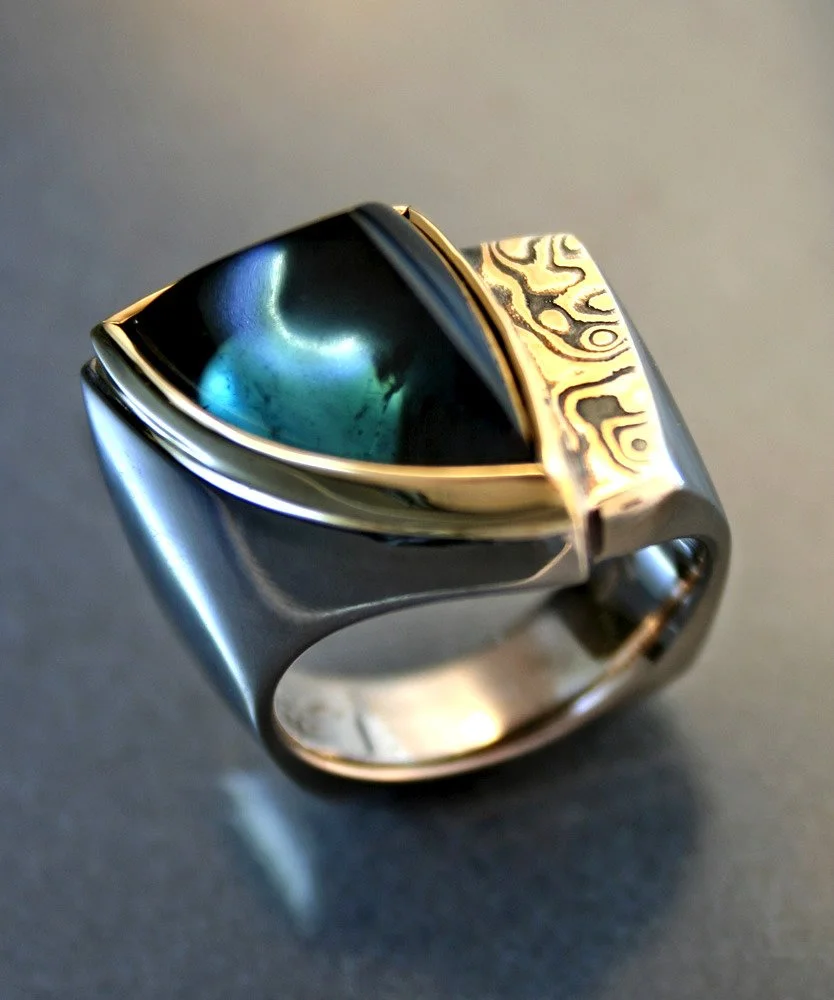 A silver and gold ring with an intricate design and a large iridescent stone set in the center.