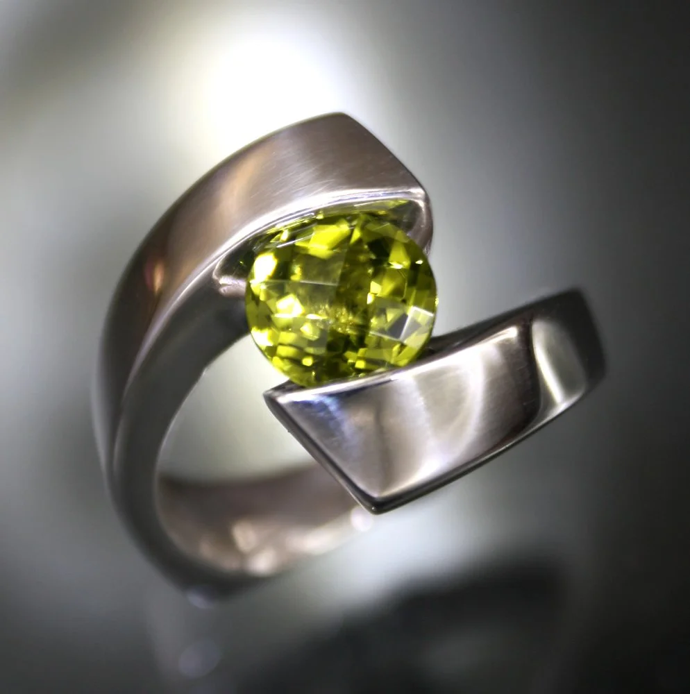 A silver ring featuring a large, oval-shaped, yellow-green gemstone set in a modern, open band design.