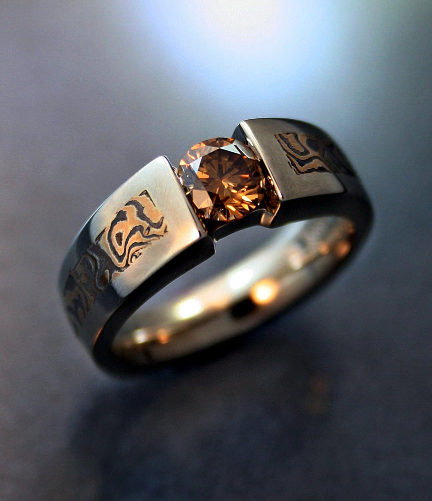 A close-up of a silver ring with a round brown gemstone in the center, resting on a dark surface.