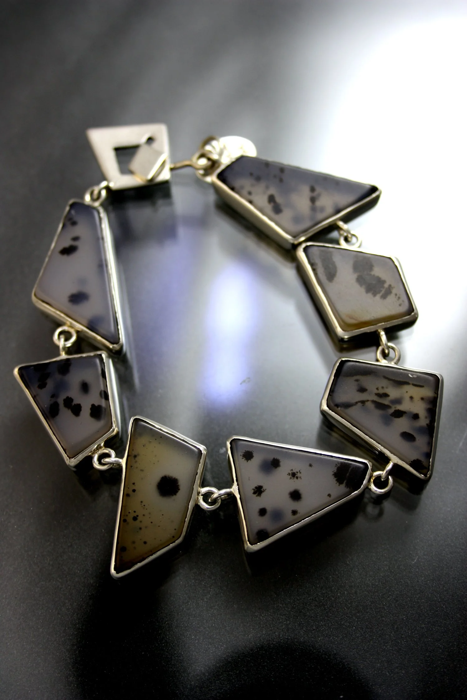 A close-up of a geometric black and white stone bracelet with a silver chain on a dark surface.
