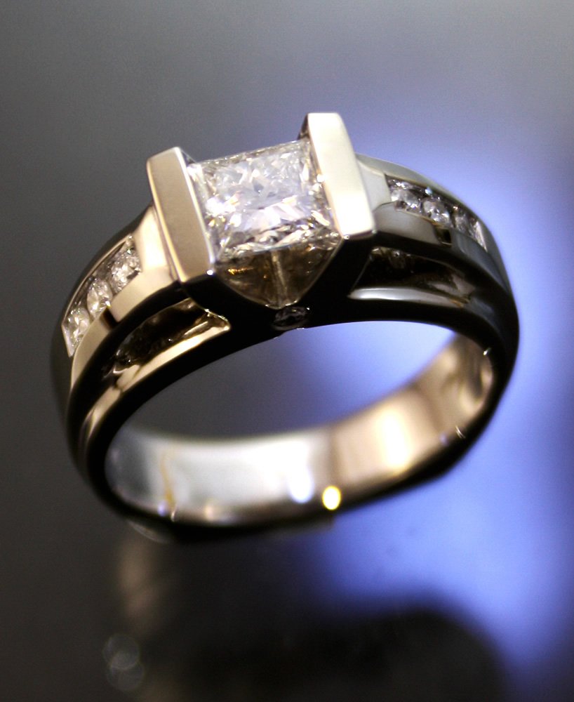 A silver ring with a large square-cut diamond in a prong setting and smaller diamonds along the band.