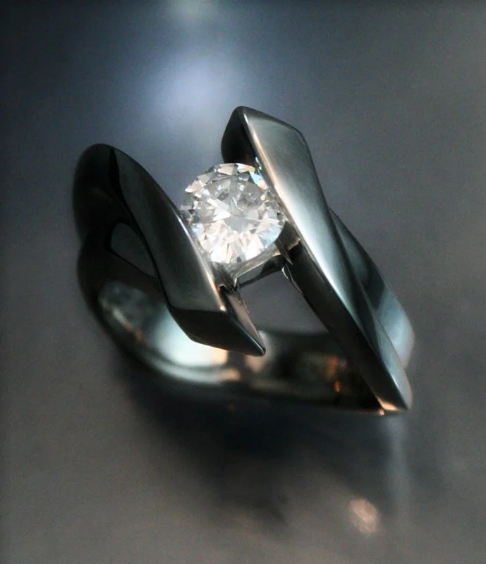 A silver ring with a large round diamond in the center, set in a modern style with a sleek and curved band.