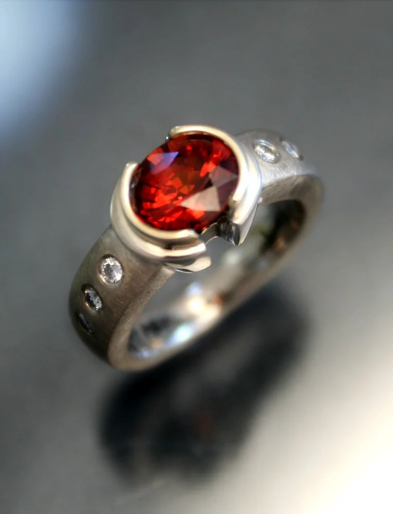 Silver ring with a large red gemstone and small diamonds embedded in the band.