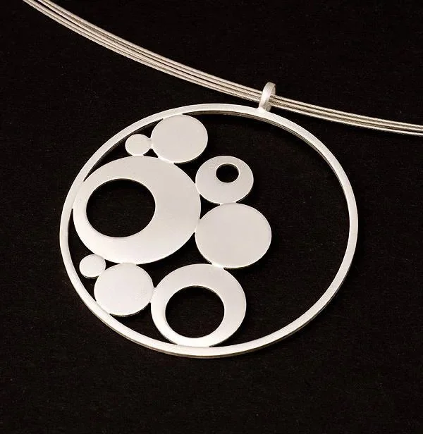 Silver necklace with a circular pendant containing various circular cutouts on a black background.