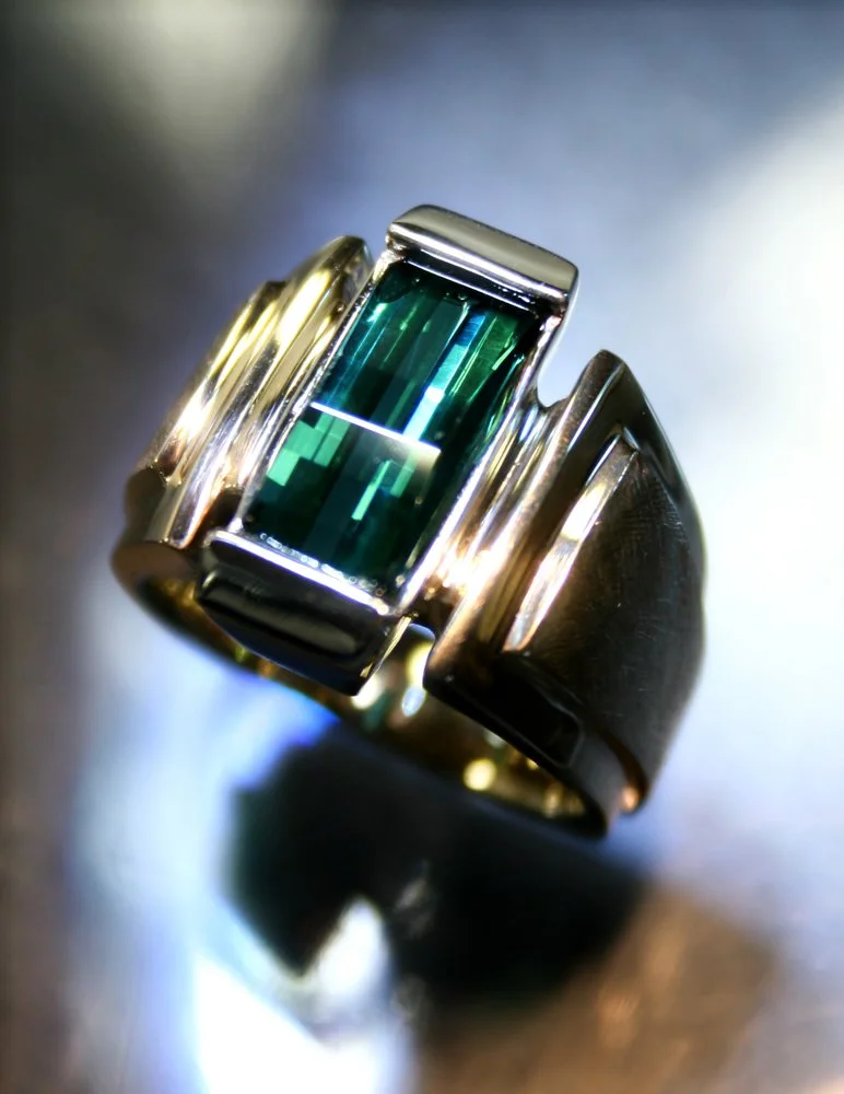 A silver ring featuring a rectangular, teal-colored gemstone with multiple facets.