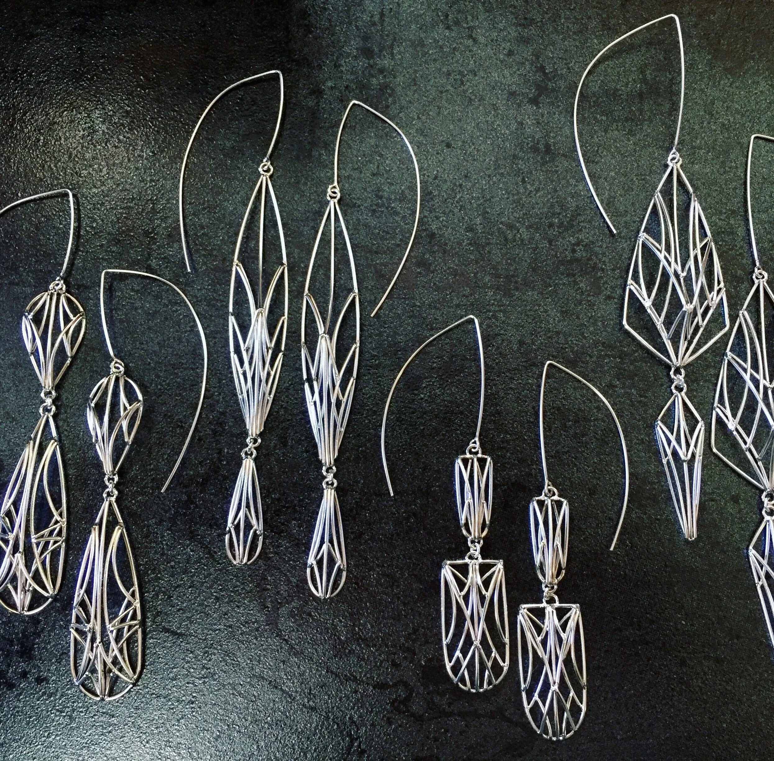 A collection of silver wire earrings with intricate geometric designs, arranged on a dark surface.