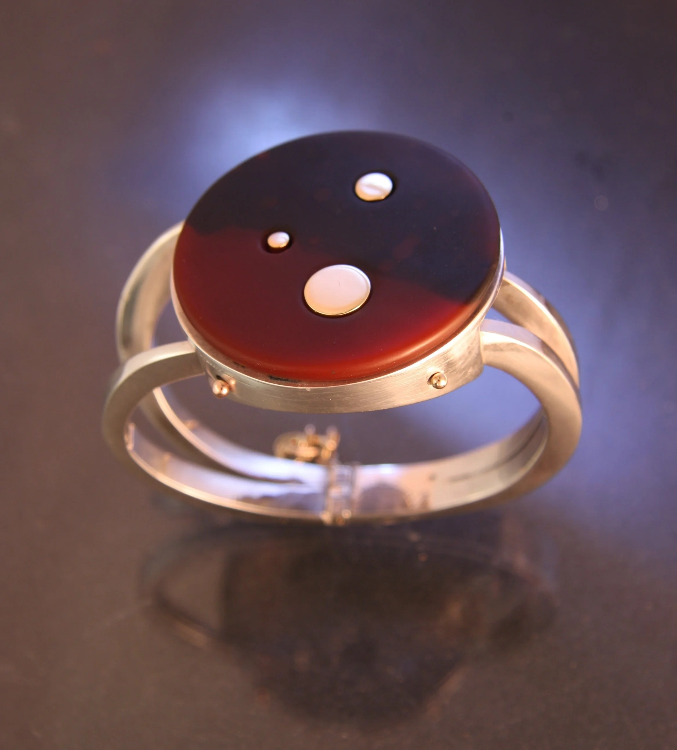 A silver ring with a round, black and red yin-yang style stone in the center, featuring two white dots of different sizes.