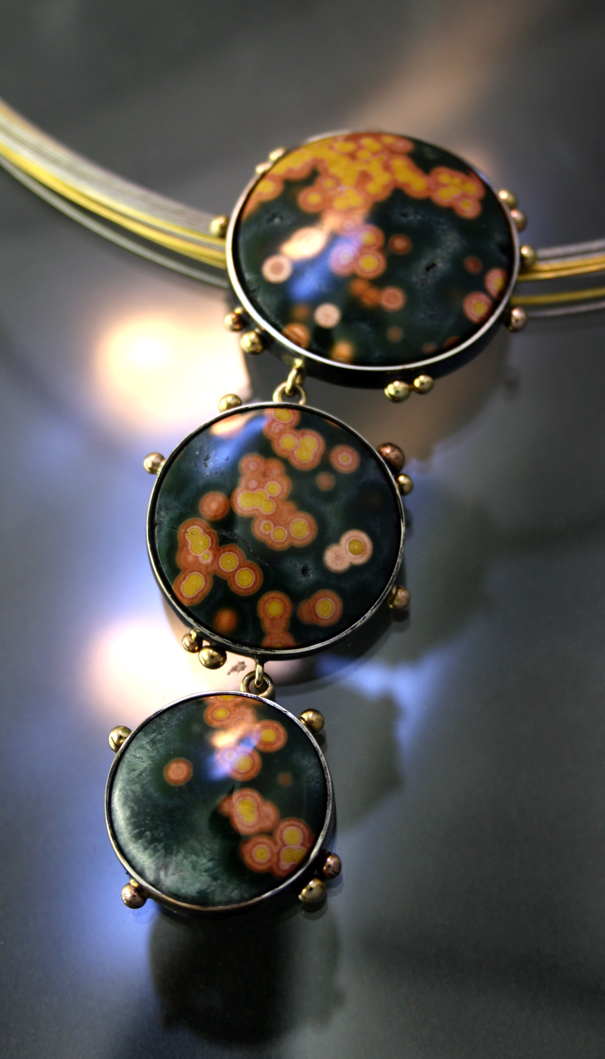 Close-up of a gold necklace with three circular stone pendants featuring a black, orange, yellow, and pink pattern.