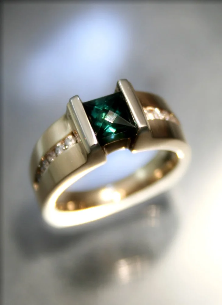 A silver ring with a square-cut green gemstone and small clear stones set along the band.