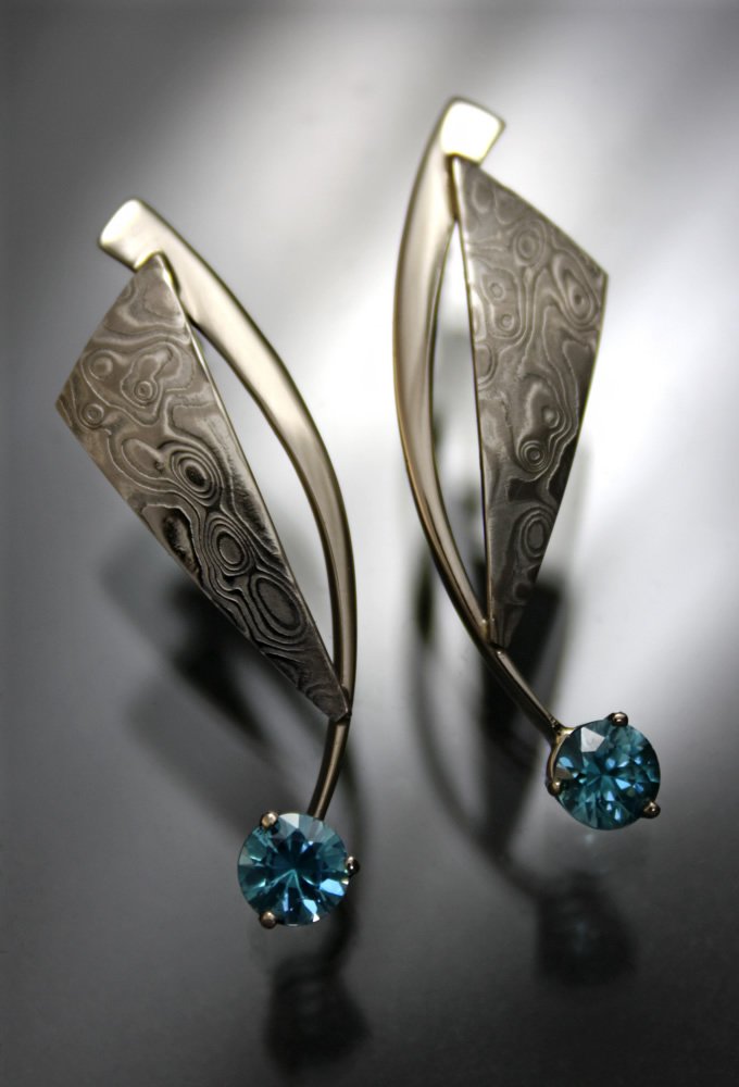 Silver earrings with a leaf design and a blue gemstone at the bottom.