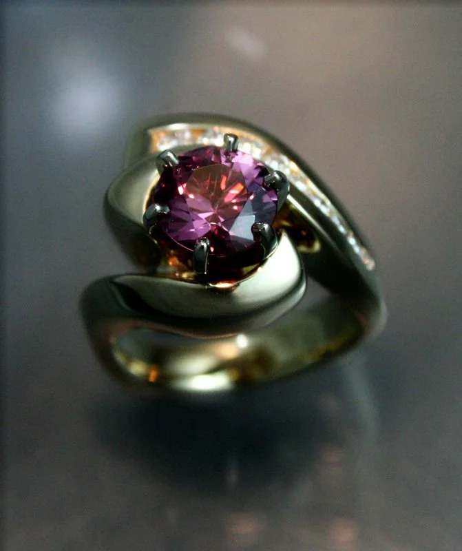 Close-up of a silver ring with a large purple gemstone and smaller white stones on the band, resting on a reflective dark surface.