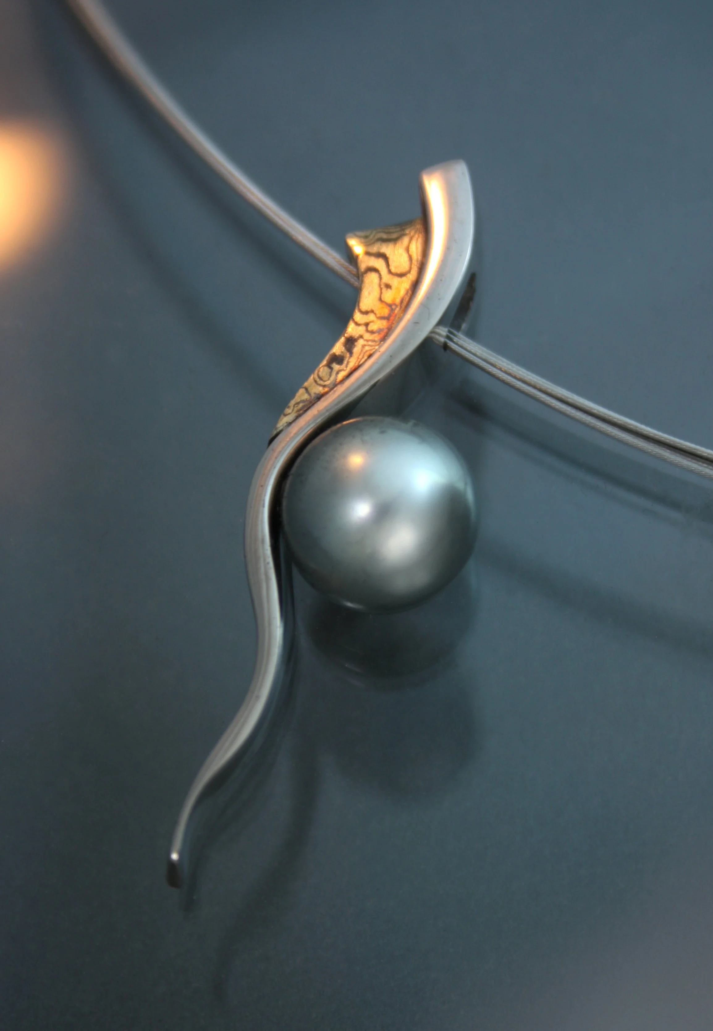 Close-up of a modern silver jewelry piece with a curved design and a spherical element on a dark background.