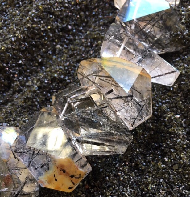 A string of clear, faceted beads with black inclusions on a dark, textured surface.