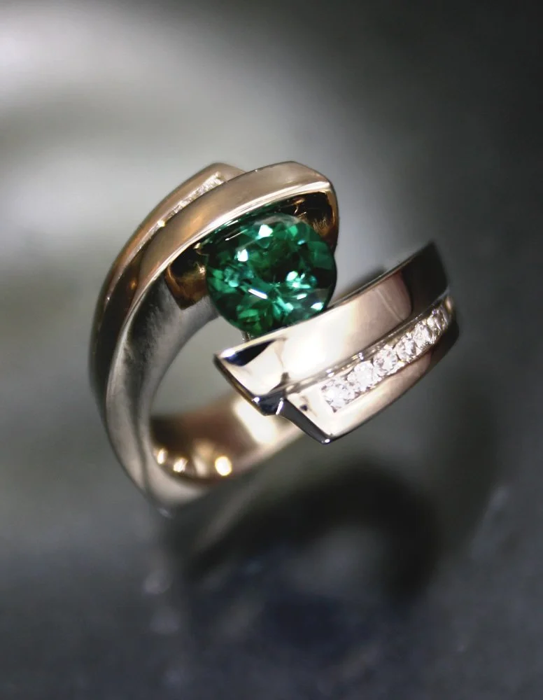 A jewelry ring with a large green gemstone and embedded small clear stones on a metallic band.