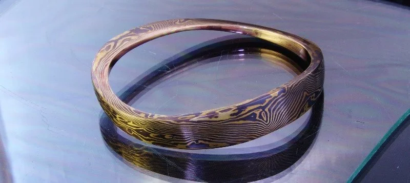 A metal necklace with a wood grain pattern printed on it, placed on a reflective surface.