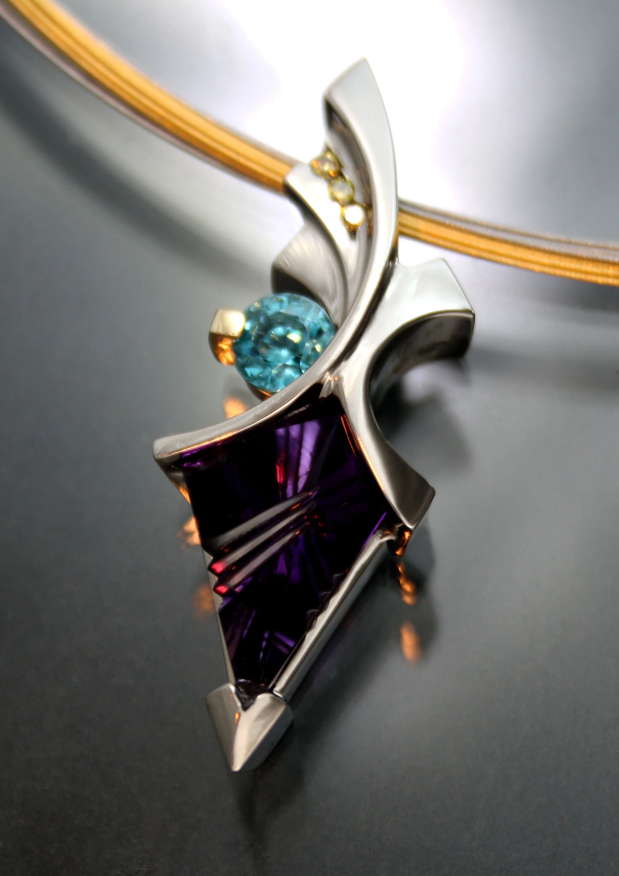 Close-up of a modern silver necklace with a colorful abstract pendant featuring a blue gemstone and a purple glass element.