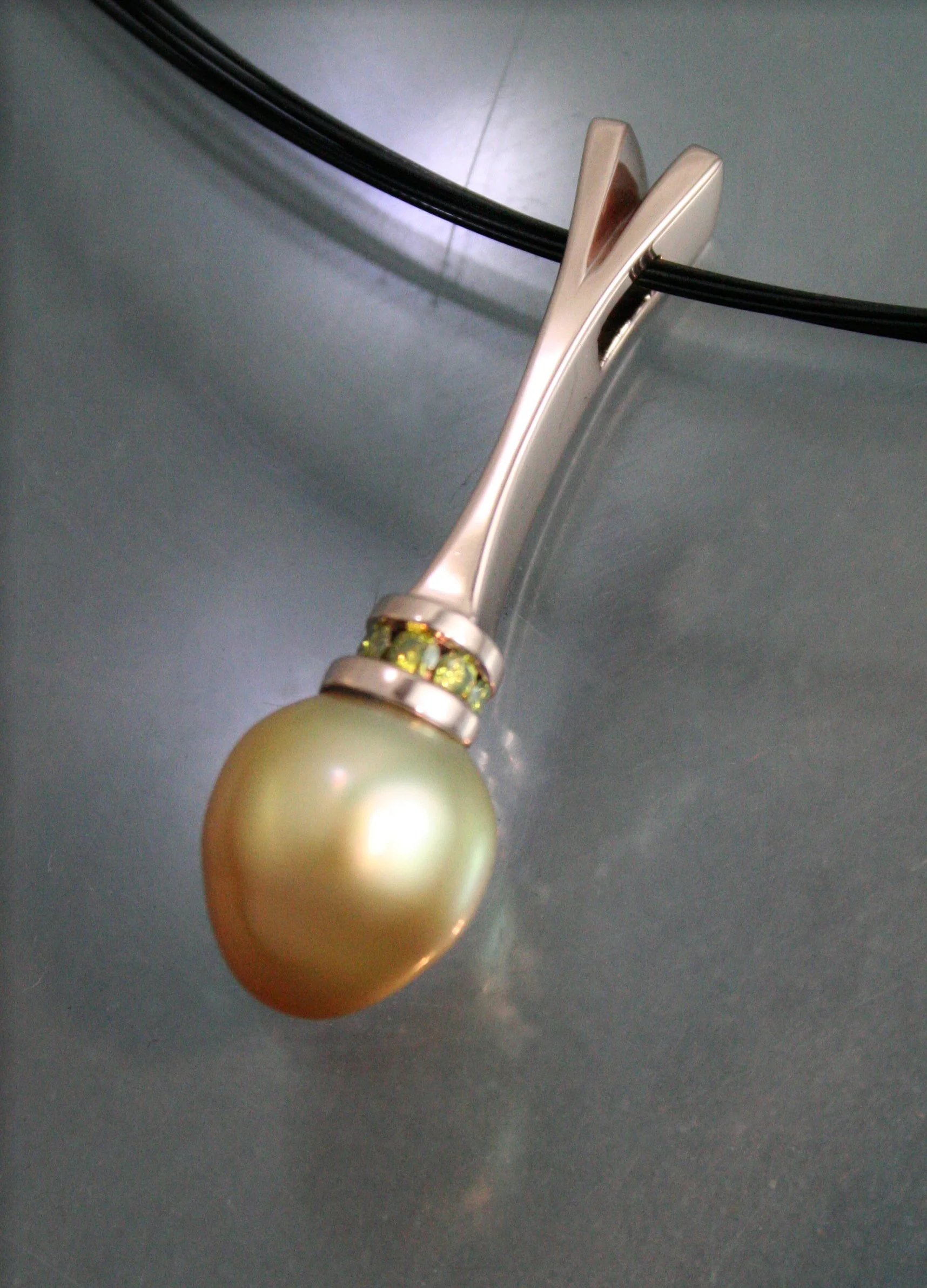 A silver hair clip with a large pearl and green gemstones on a grey surface.