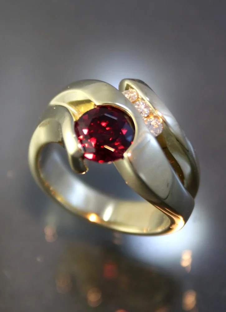 A gold and silver ring with a large red gemstone in the center and small clear stones on the side.