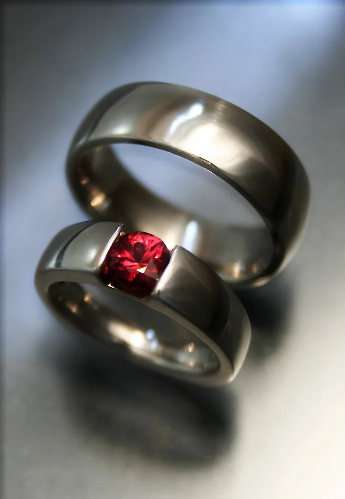 Two silver rings, one with a red gemstone, intertwined and placed on a gray surface.