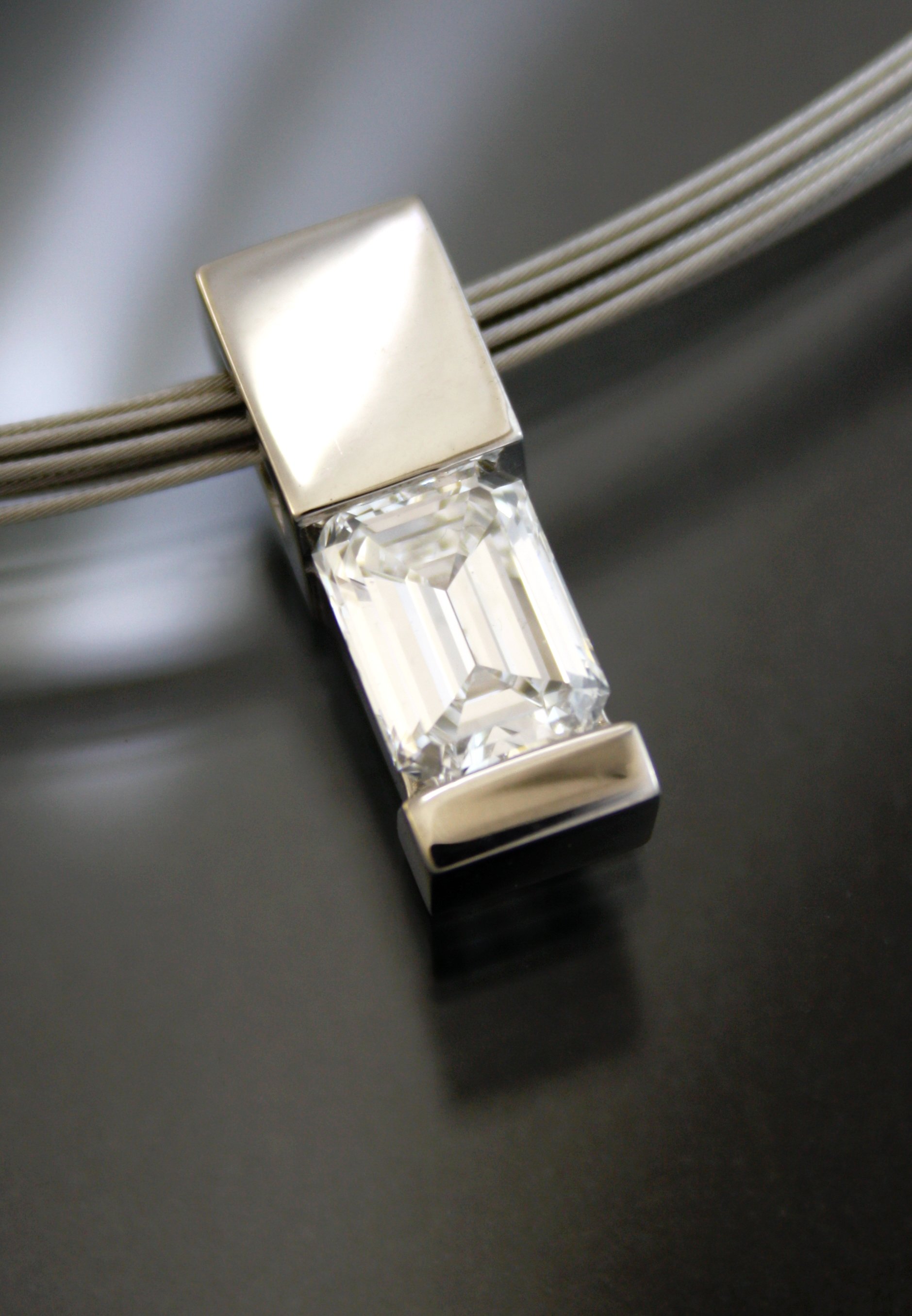 A jewelry pendant featuring a large rectangular emerald-cut gemstone set in a silver or white gold frame, attached to a multi-strand metallic necklace.