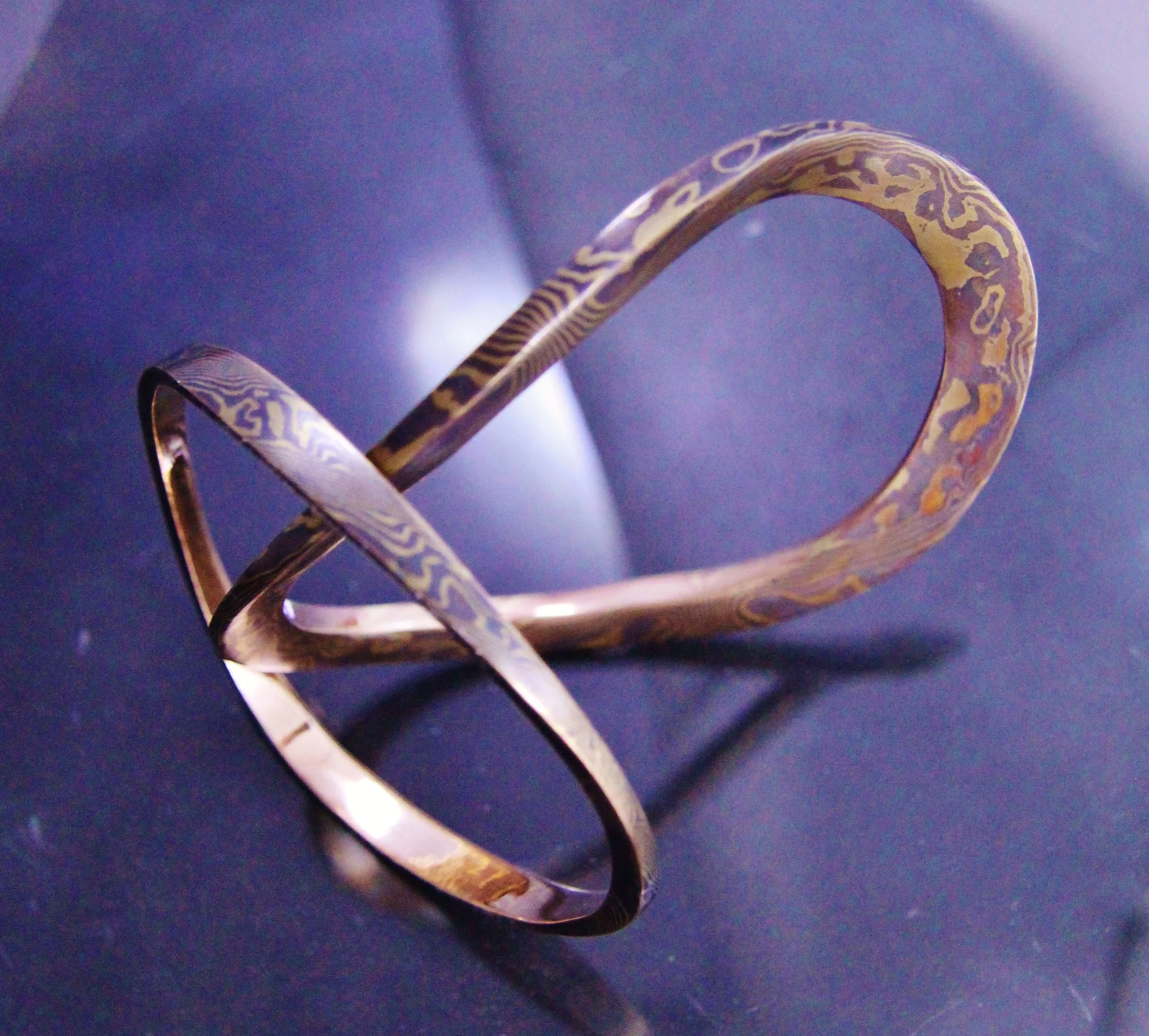 A twisted, patterned metallic bracelet on a dark surface.