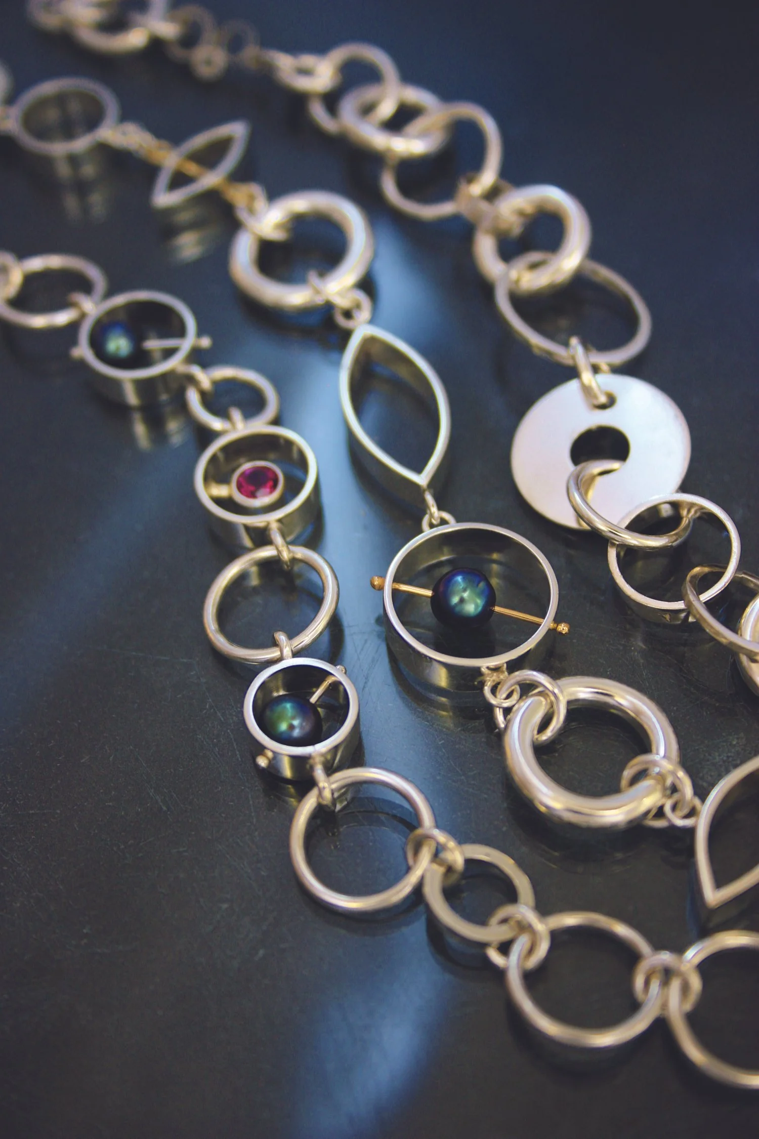 Various silver jewelry pieces including necklaces, earrings, and rings with colorful beads and gemstones on a dark surface.