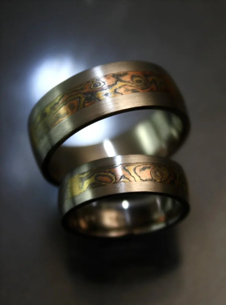 Two metallic rings with a woodgrain pattern design placed on a dark surface.