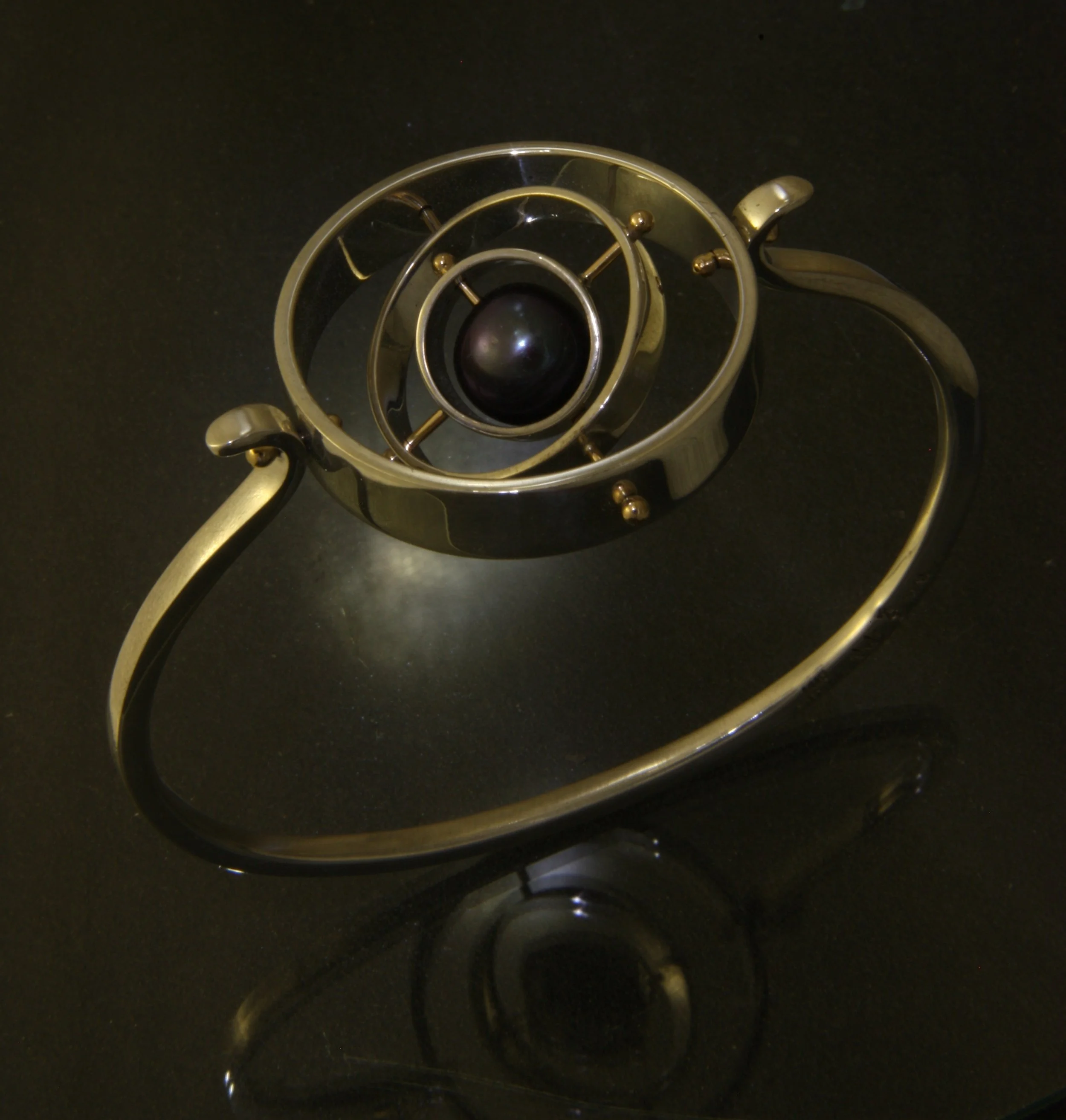 A metallic spiral bracelet with a black central stone, lying on a reflective black surface.