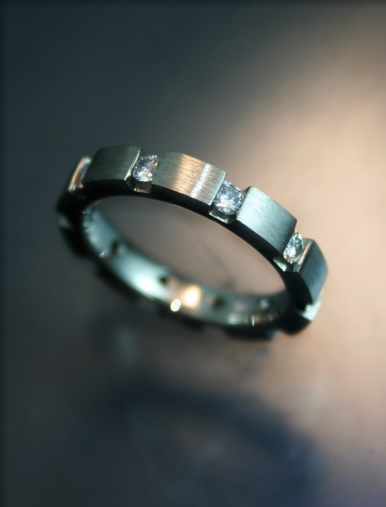 Silver ring with embedded diamonds on a dark surface.