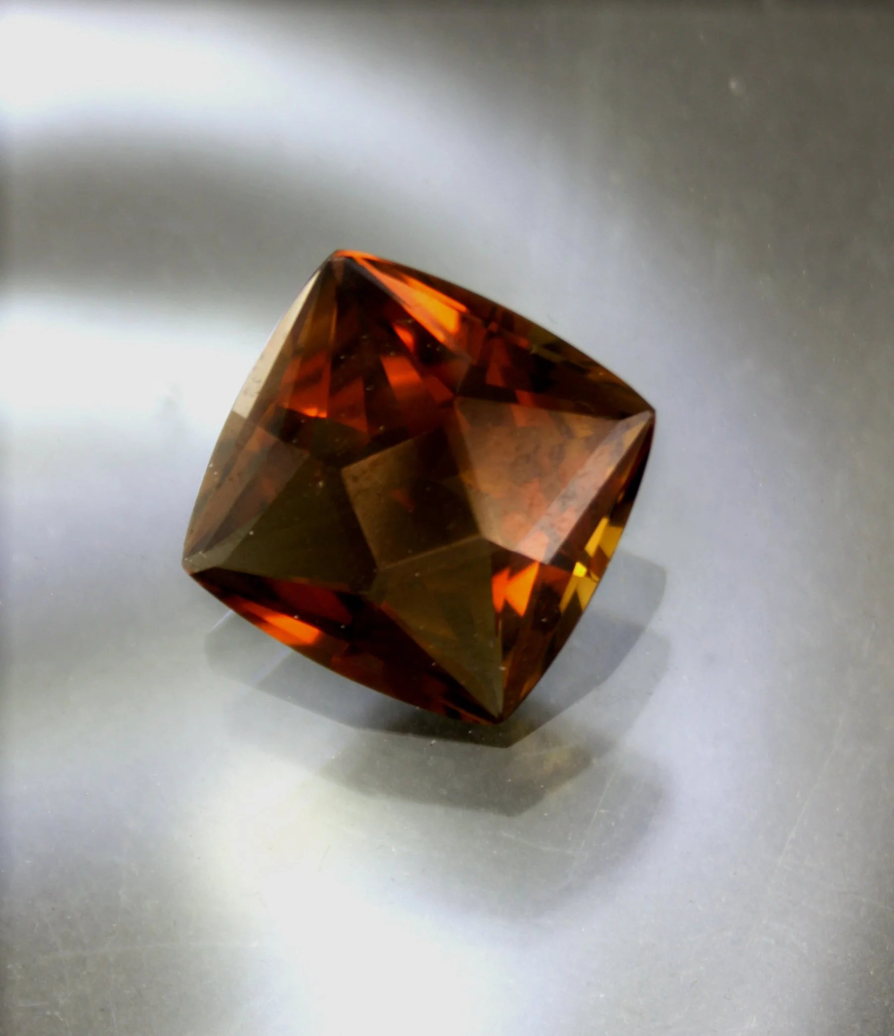 A small, faceted, brownish-orange gemstone on a reflective surface.