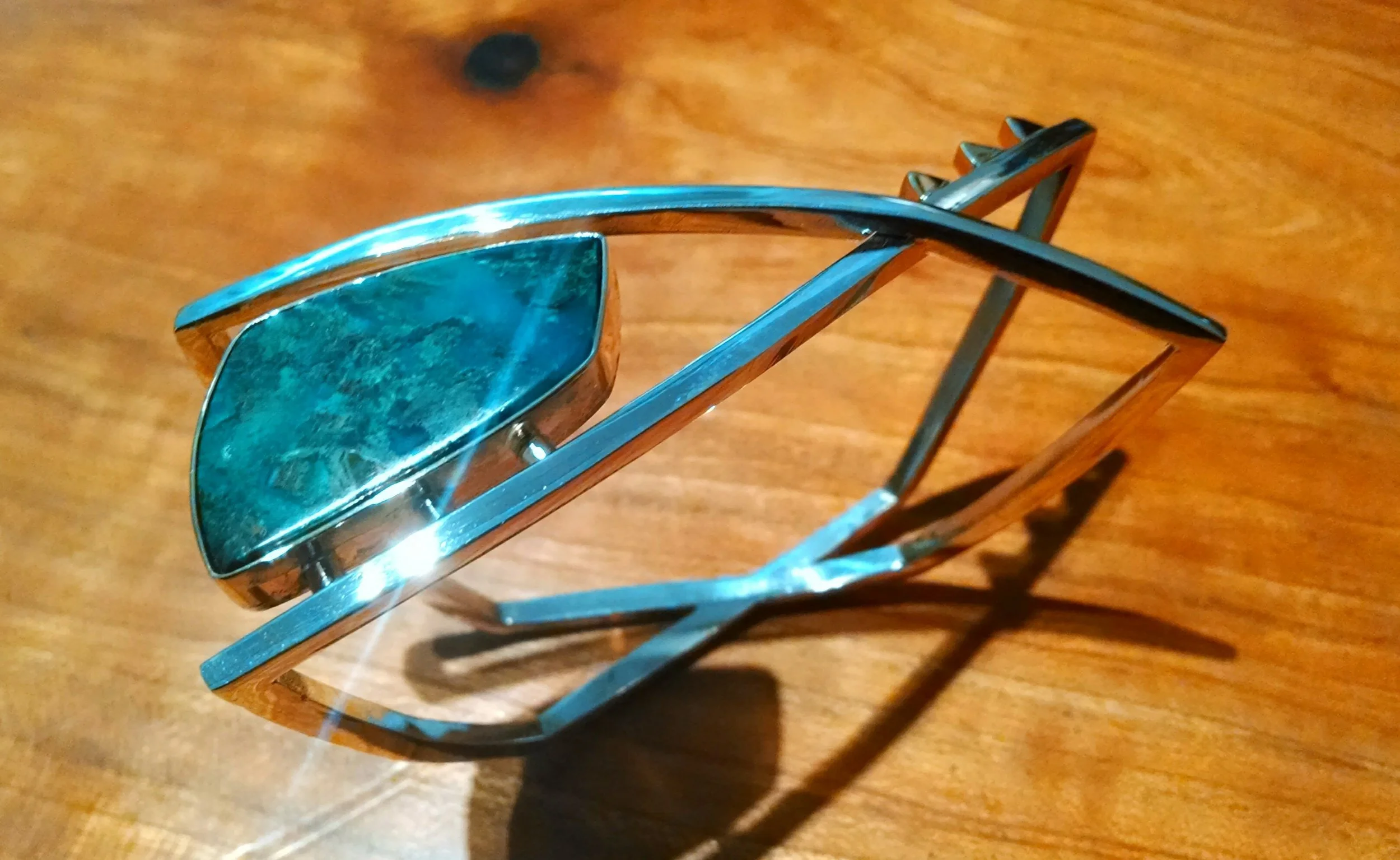 Silver bracelet with three blue-green stones lying on a wooden surface.