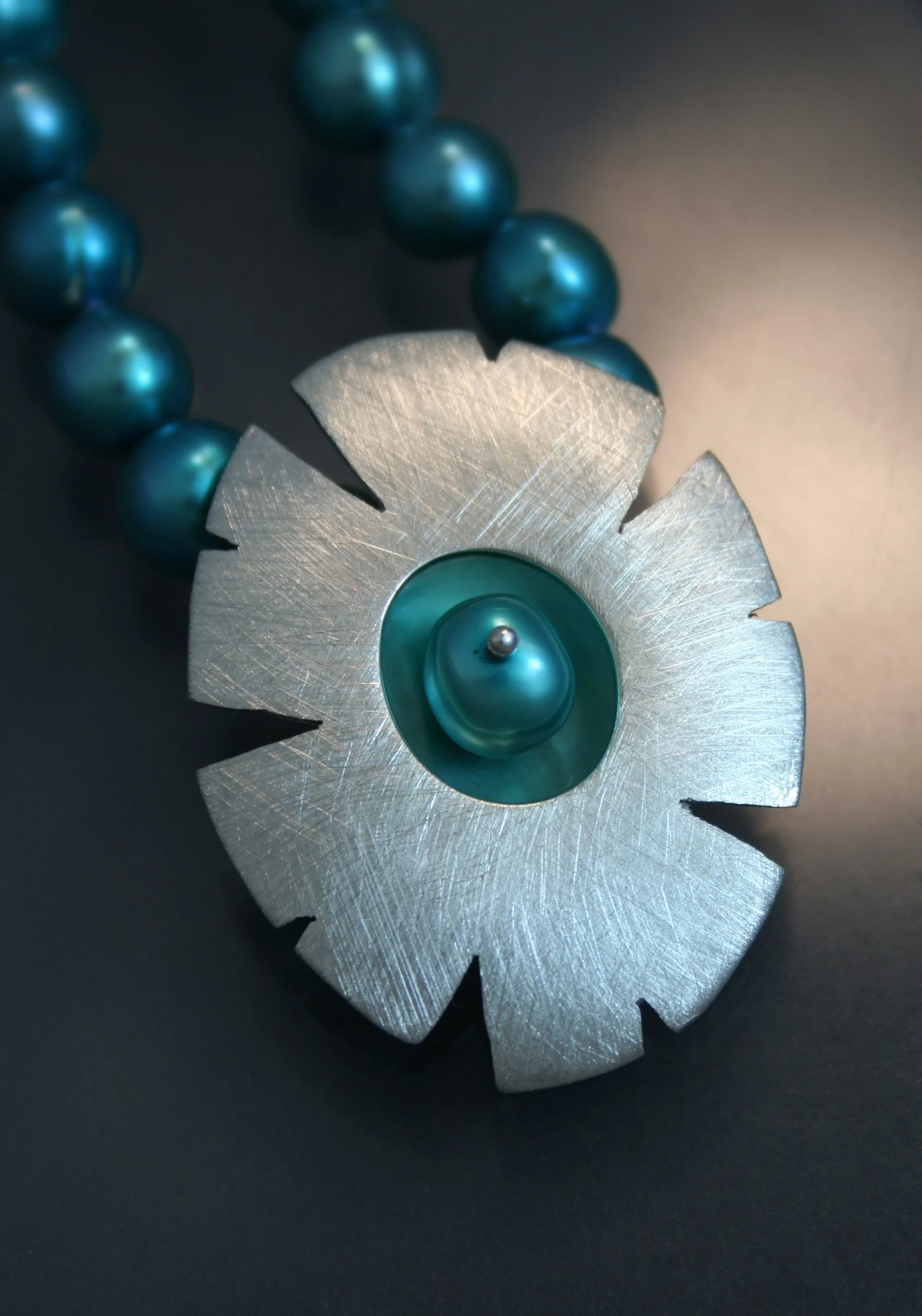 A necklace with blue beads and a large silver flower-shaped pendant with a blue center and a pearl on top.