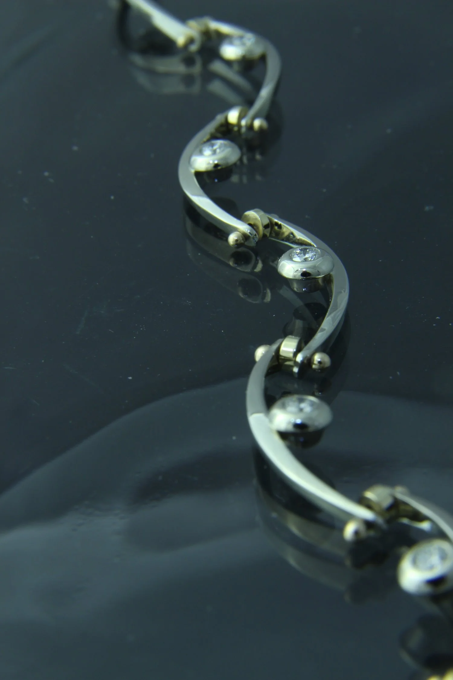Close-up of a silver bracelet with embedded gemstones on a dark, reflective surface.