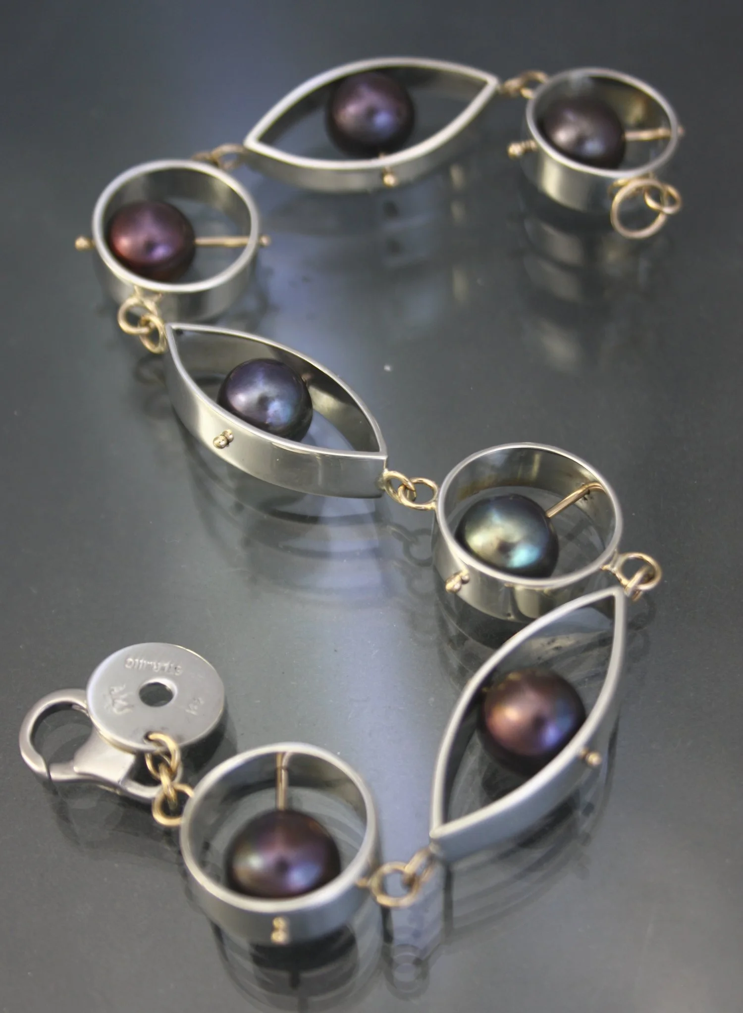 Silver jewelry with black and dark purple pearls on a black surface.