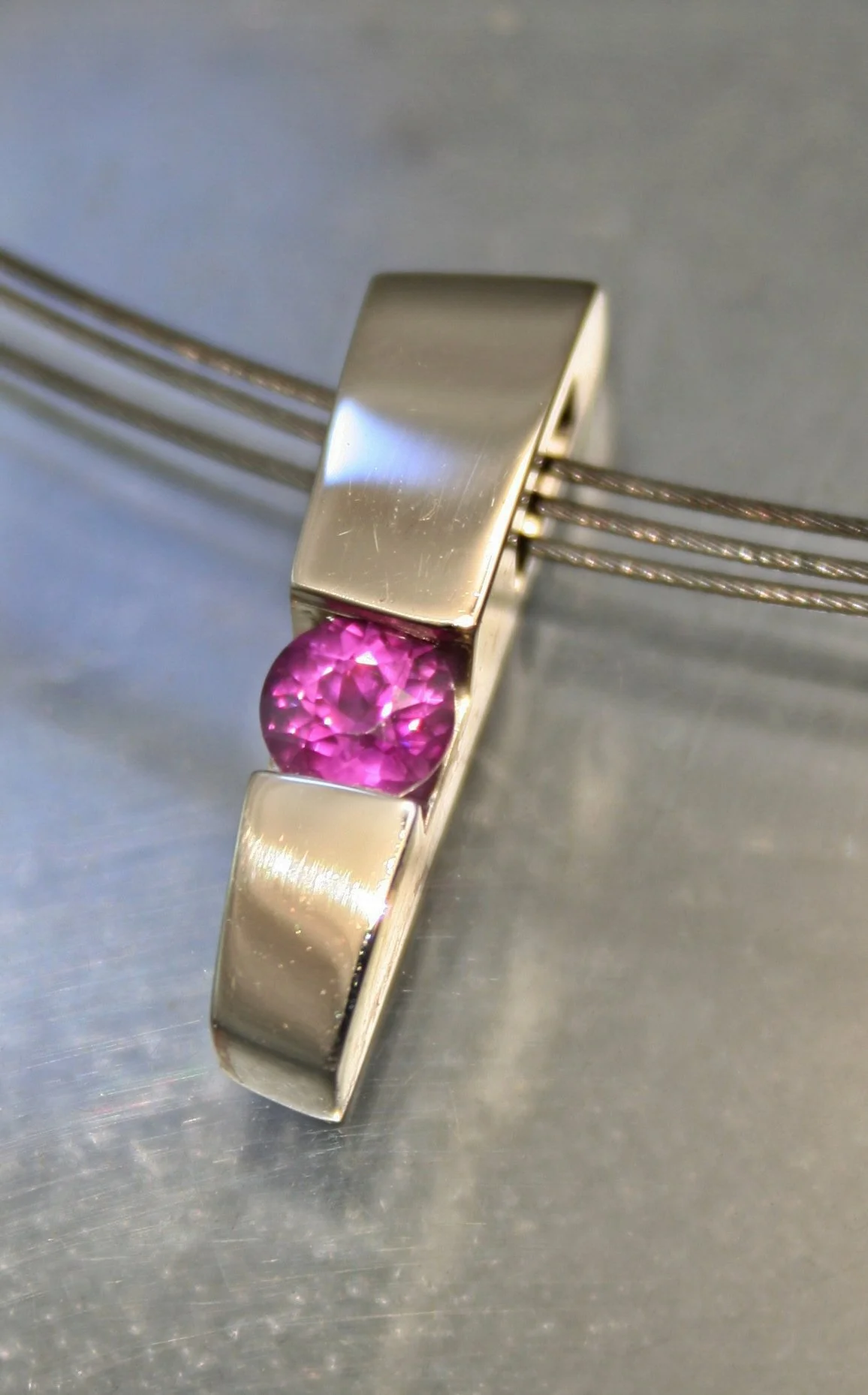 A silver ring with a pink gemstone set in the center, designed with two rectangular bands on either side.