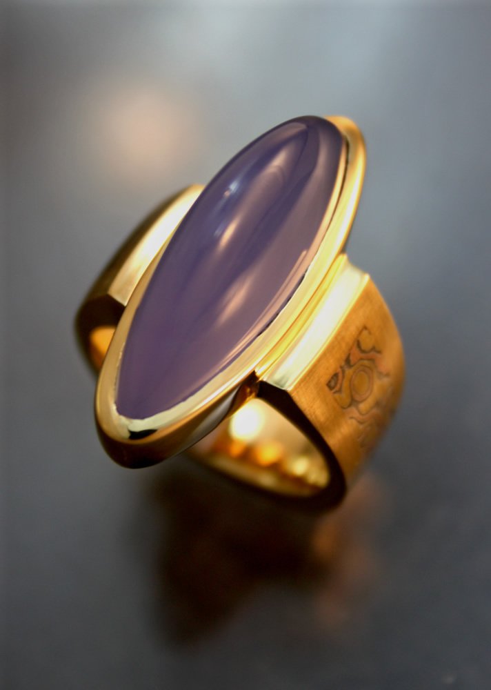 Gold ring with a large, oval, purple gemstone in the center.