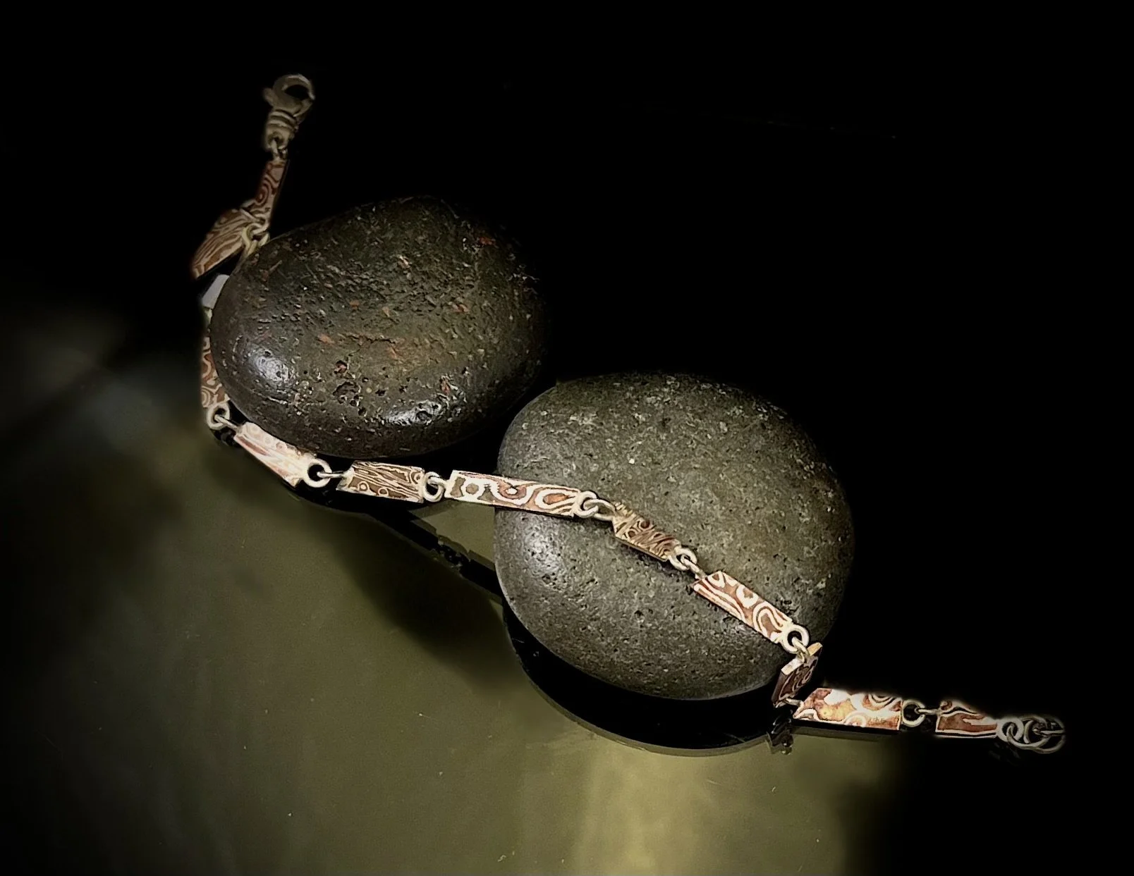 Close-up of two smooth, dark gray rocks submerged in water, with a decorative metal chain resting on top of them.
