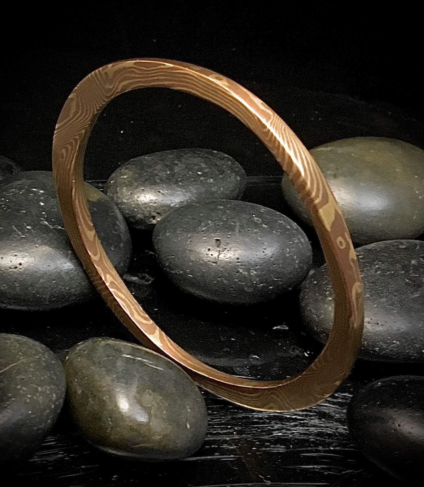 A gold ring resting on black stones with a dark background.